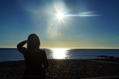 Rear view of woman standing at beach against sky during sunset