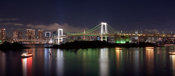 Illuminated bridge over river in city against sky at night