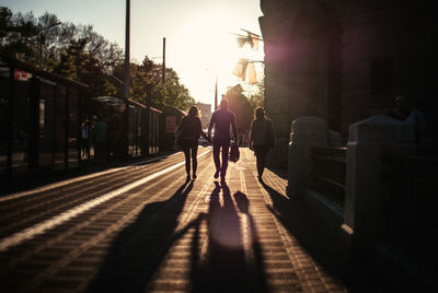 Silhouette of three people walking on sidewalk