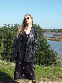 Young woman wearing sunglasses standing by plants against sky