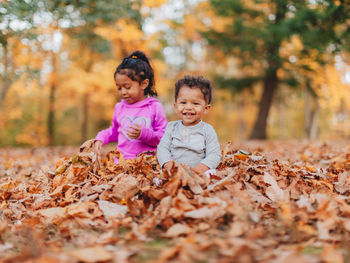 Smiling kids sitting on autumn leaves outdoors