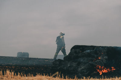 Side view of man standing on rock against sky