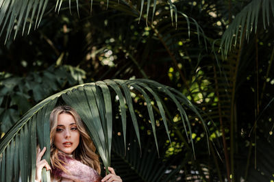 Portrait of woman standing against palm tree