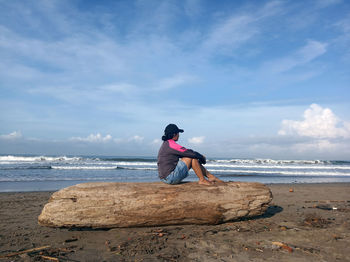 Man sitting on rock at beach against sky