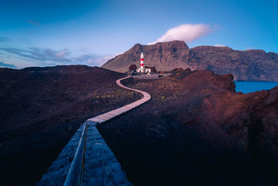 Winding pathway leading to beacon located on hill near sea on background of mountains in morning in tenerife