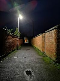 Illuminated street amidst buildings against sky at night