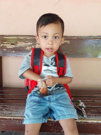 Portrait of cute boy sitting on bench outdoors