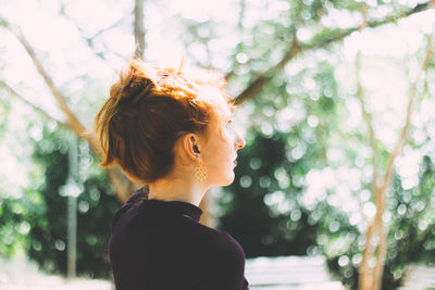 Side view of young woman against trees