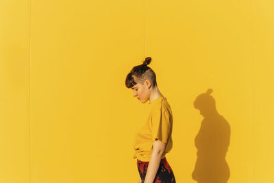 Androgynous person with half-shaved hairstyle standing by yellow wall