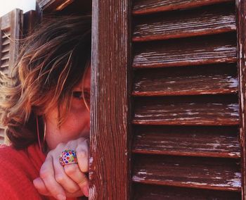 Portrait of woman hiding by wooden door