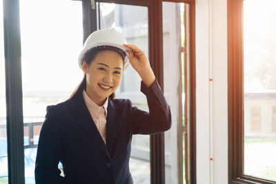 Portrait of smiling young woman standing against window