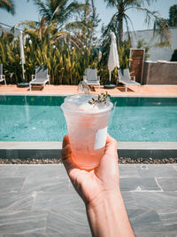 Cropped image of hand holding drink by swimming pool