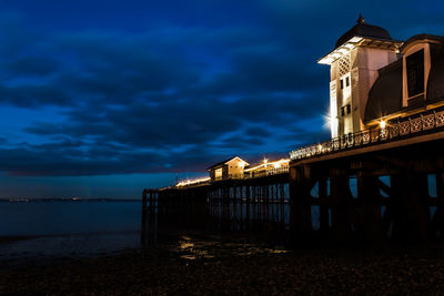 Illuminated building by sea against sky at night