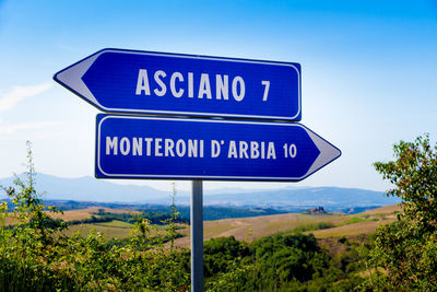 Road sign by trees against blue sky