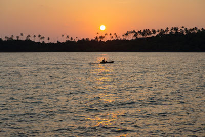 Silhouette man in sea against sky during sunset