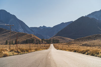 Two lane road in the arid sierra nevada's california leading to mountains against clear blue sky.