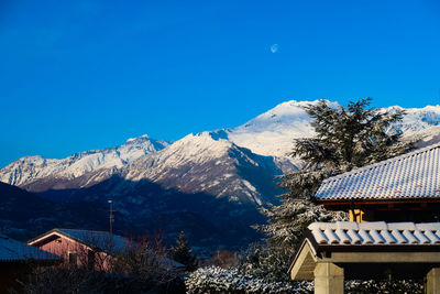 Houses by snowcapped mountains against clear blue sky