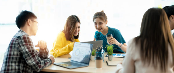 Side view of friends using laptop at office