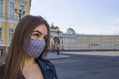 Portrait beautiful young woman in medical mask on palace square in st. petersburg. positive 