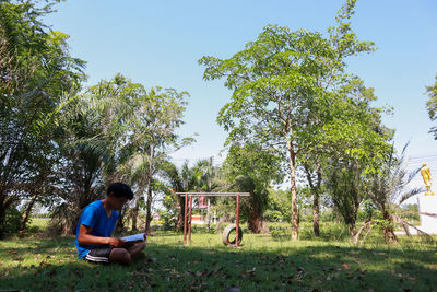 Man sitting on field against trees