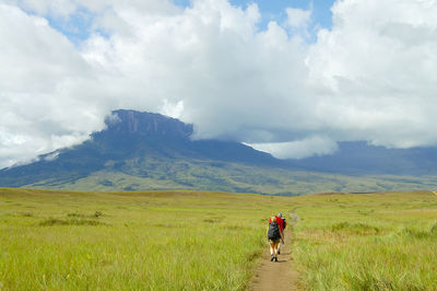 Rear view of people walking on field against sky