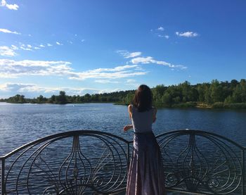 Rear view of woman standing by railing against lake