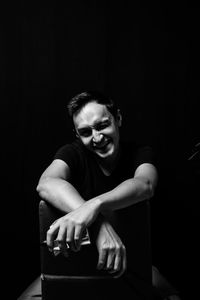 Portrait of smiling young man sitting against black background