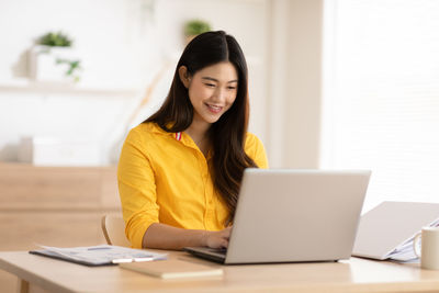 Young woman using phone while sitting on table