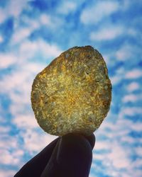 Close-up of hand holding rock against sky