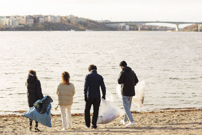 Rear view of environmentalists with microplastics garbage walking against lake