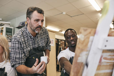 Young man discussing over canvas with tutor in art class