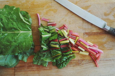 Directly above shot of chopped rhubarb leaves with knife on wooden table