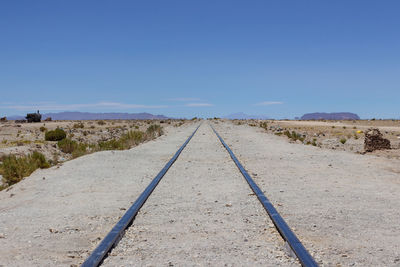 Railroad track amidst land against clear blue sky