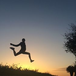 Low angle view of silhouette mid adult man jumping against clear sky during sunset