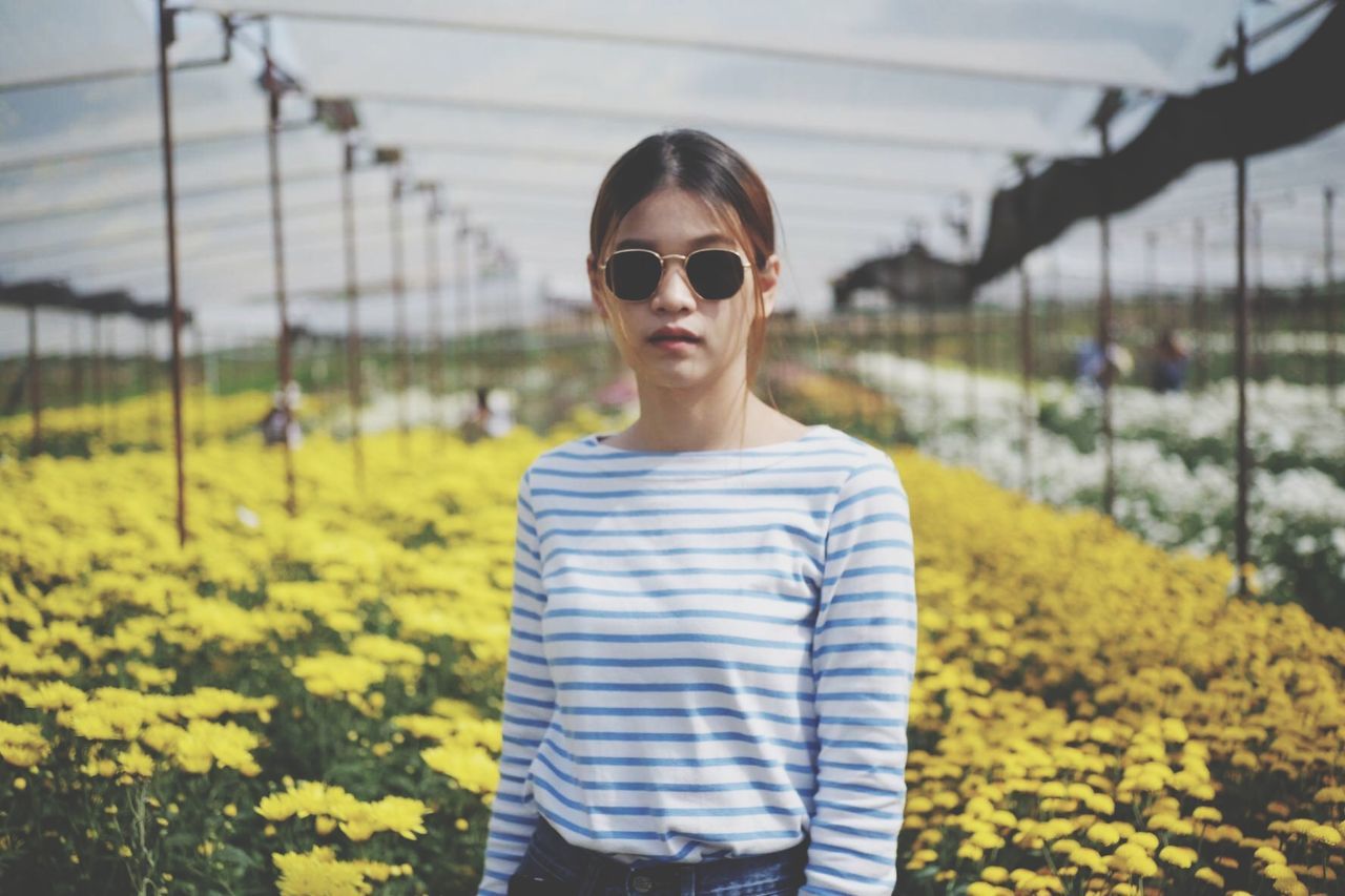 one person, sunglasses, glasses, real people, front view, portrait, waist up, standing, focus on foreground, plant, day, fashion, nature, leisure activity, lifestyles, young adult, looking at camera, field, protection, outdoors, hairstyle, beautiful woman