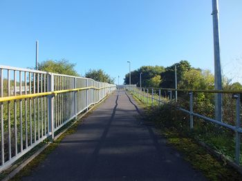 Walkway amidst trees against clear blue sky