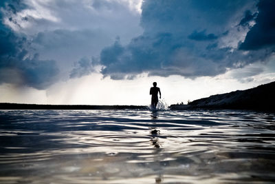 Silhouette man standing in sea against sky