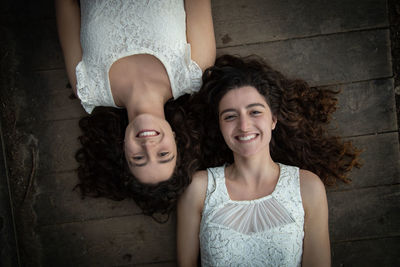 Directly above portrait of smiling twin sisters lying down on boardwalk