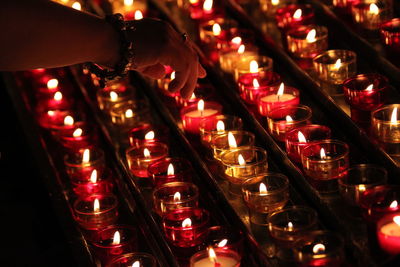 Cropped hand of woman over tea lights candles in darkroom