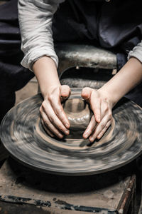 Midsection of man shaping earthenware on pottery wheel