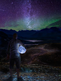 Digital composite image of man holding moon while standing on rock against sky at night
