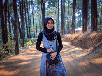 Portrait of smiling young woman standing amidst trees