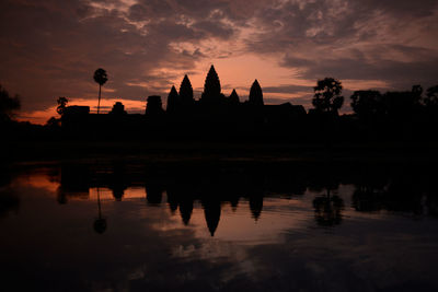 Reflection of silhouette built structure and trees in lake against sky during sunset