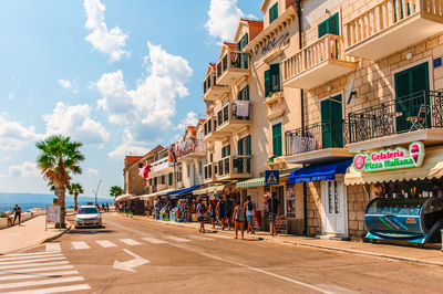 People on street amidst buildings in city against sky