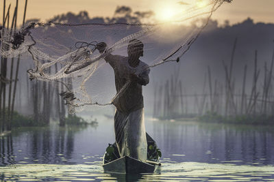 Man fishing in lake against sky during sunset