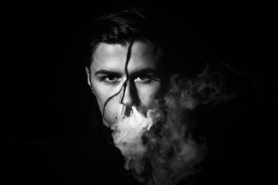 Close-up portrait of young man smoking against black background