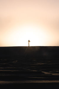 Silhouette man standing by sea against sky during sunset