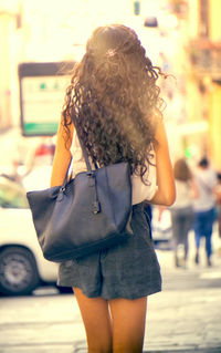 Rear view of young woman carrying purse while standing on street