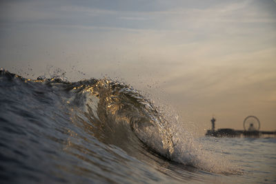 Waves splashing in sea against sky at sunset