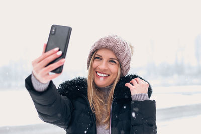 Portrait of smiling young woman using smart phone during winter